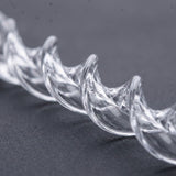 A clear acrylic Christmas ornament shaped like a spiral icicle lies diagonally on a dark gray textured surface, showing curved ridges.