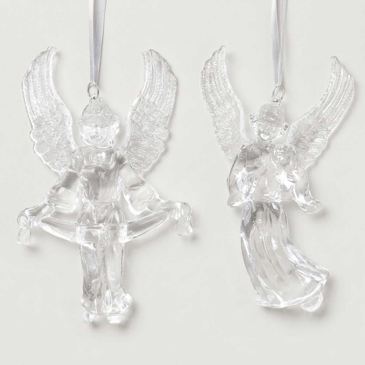 Two clear acrylic angel Christmas ornaments with raised textured wings hang from white ribbons against a white background.