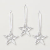 Three clear acrylic five-point star Christmas ornaments with faceted surfaces and white hanging ribbons are arranged against a white background.