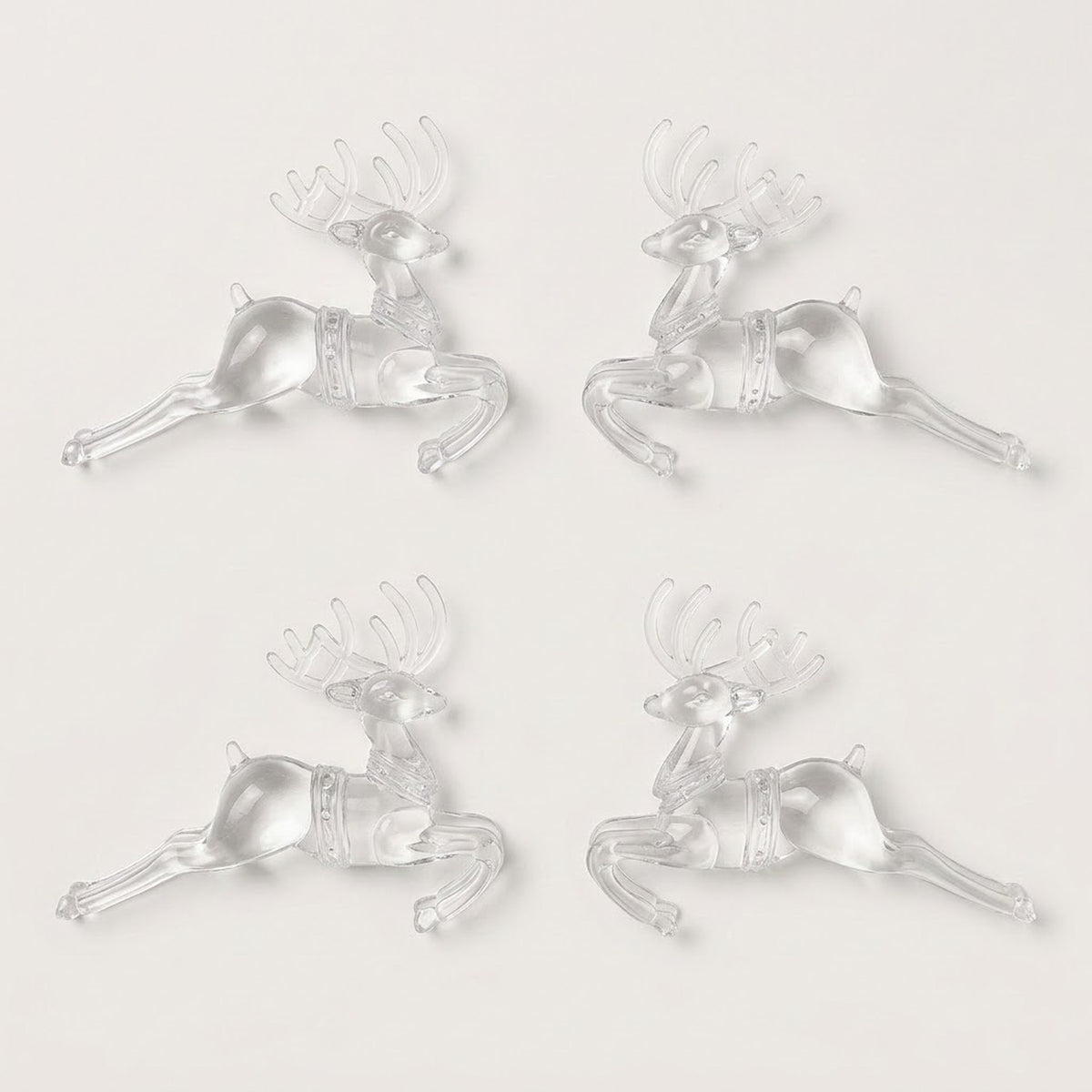 Four clear acrylic leaping reindeer Christmas ornaments with antlers are arranged in two inward-facing pairs against a white background.