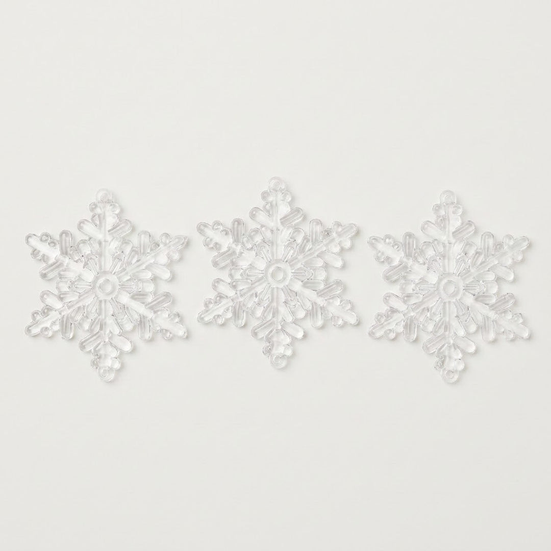 Three clear acrylic snowflake Christmas ornaments with six branching points sit side by side on a white background.