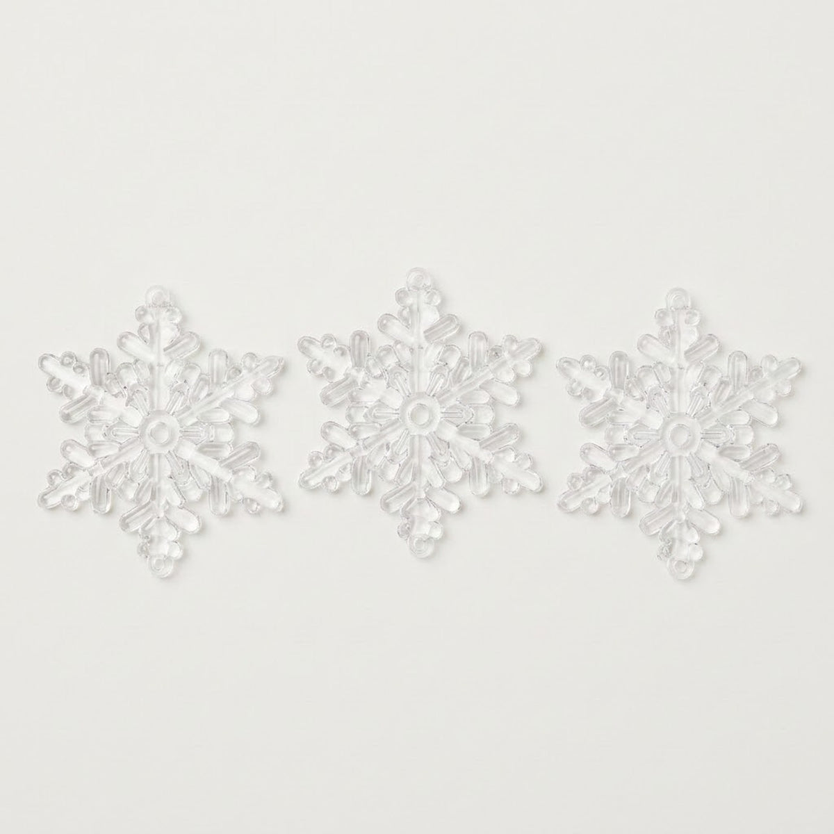Three clear acrylic snowflake Christmas ornaments with six branching points sit side by side on a white background.