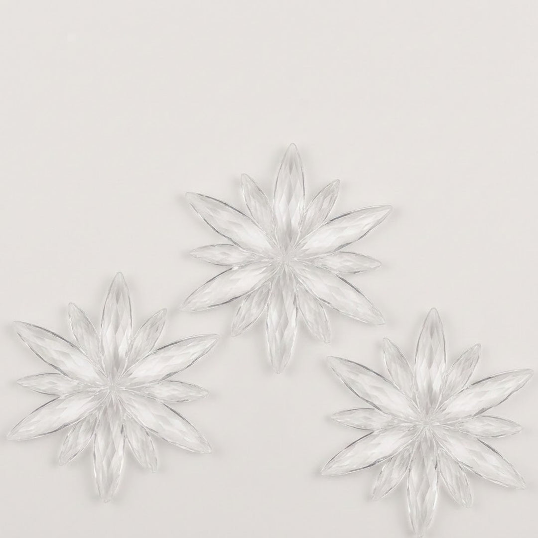Three clear acrylic starburst Christmas ornaments with long pointed rays form a triangular arrangement on a white background.