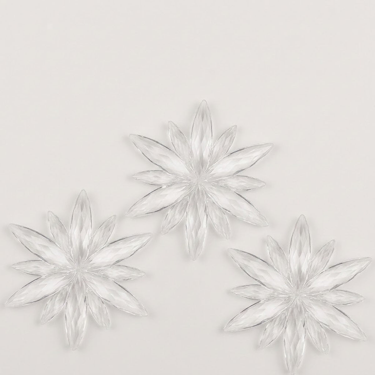 Three clear acrylic starburst Christmas ornaments with long pointed rays form a triangular arrangement on a white background.