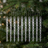 Ten clear spiral icicle ornaments hang from silver cords on evergreen branches against a dark green background.