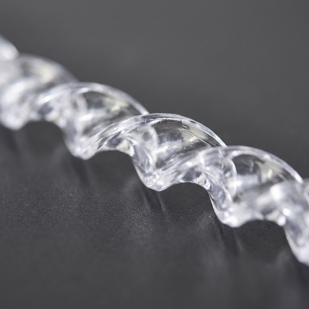 A close-up shows the curved, transparent spiral surface of an icicle ornament resting diagonally on a dark gray surface.