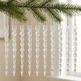Ten clear spiral icicle ornaments hang in a row from silver cords beneath an evergreen branch against a bright indoor background.