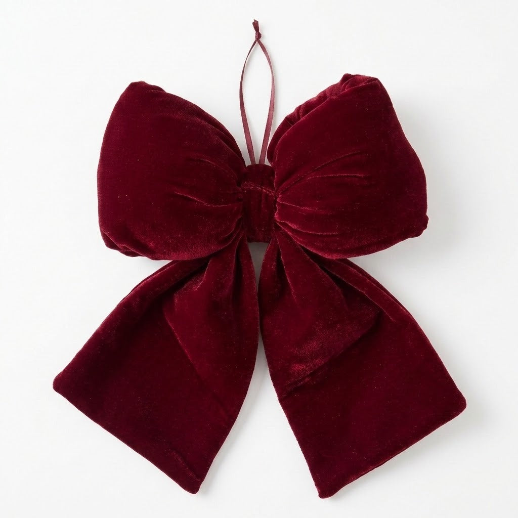 A wine red velvet Christmas bow with broad gathered loops, two tails, and a thin hanging loop rests on a white background.