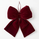 A wine red velvet Christmas bow with broad gathered loops, two tails, and a thin hanging loop rests on a white background.