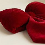 A red velvet Christmas bow rests on a cream surface, with its textured loops, wrapped center, and folded tail shown close up.