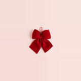 A red velvet Christmas bow with two broad tails and a ribbon hanging loop sits centered on a spacious pale pink background.