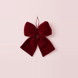 A wine-red velvet Christmas bow with broad tails and a thin hanging loop rests against a pale pink background.