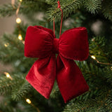 A bright red velvet bow hangs by a red cord among green Christmas tree branches and warm white lights.