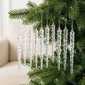 Clear textured icicle ornaments hang from silver cords on green Christmas tree branches against a softly blurred cream interior.