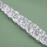 A close-up shows the irregular faceted surface of a clear icicle ornament lying diagonally on a muted green background.