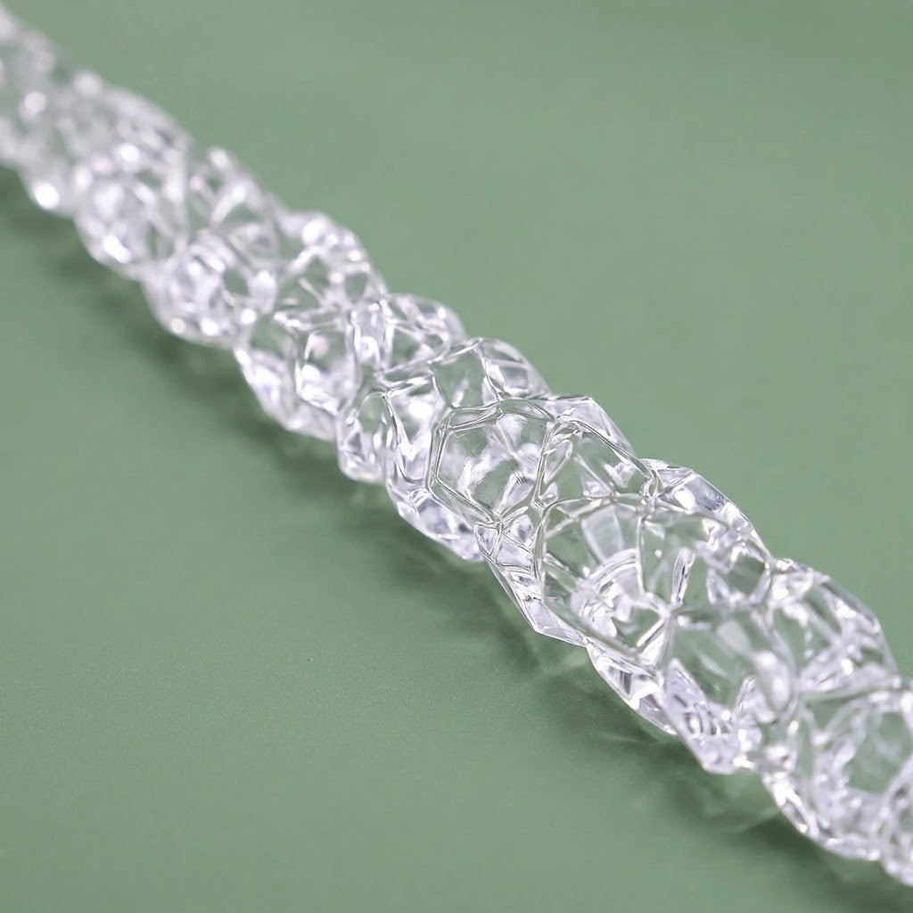 A close-up shows the irregular faceted surface of a clear icicle ornament lying diagonally on a muted green background.