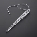 A clear faceted icicle ornament with a transparent hanging cord lies diagonally on a dark gray background.