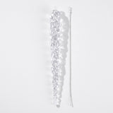 A clear tapered icicle ornament lies beside a separate silver hanging cord on a white background, casting a soft shadow.