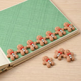 Brown resin gingerbread craft embellishments with red bows and pale blue buttons line a green scrapbook page, with three on the wooden surface.