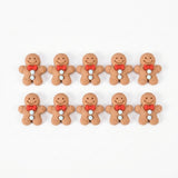 Ten brown resin gingerbread craft embellishments with red bows and pale blue buttons form two rows on a white background.