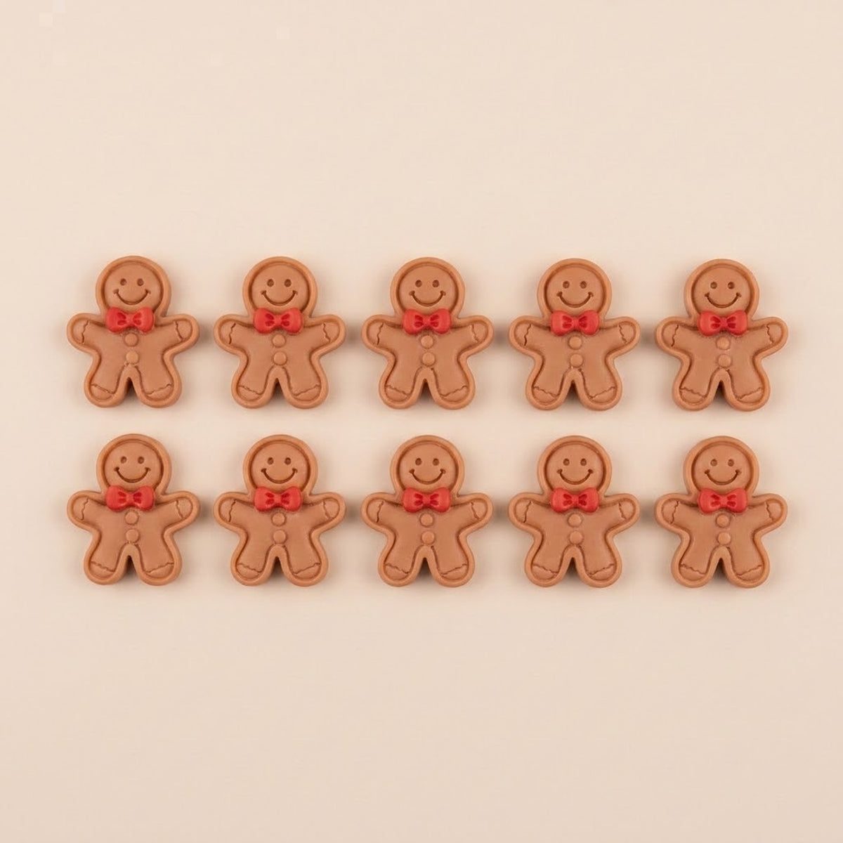 Ten brown resin gingerbread craft embellishments with outlined edges, red bows, and brown buttons sit in two rows against beige.
