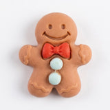 A brown resin gingerbread craft embellishment has a smiling face, red bow tie, and pale blue buttons against white.