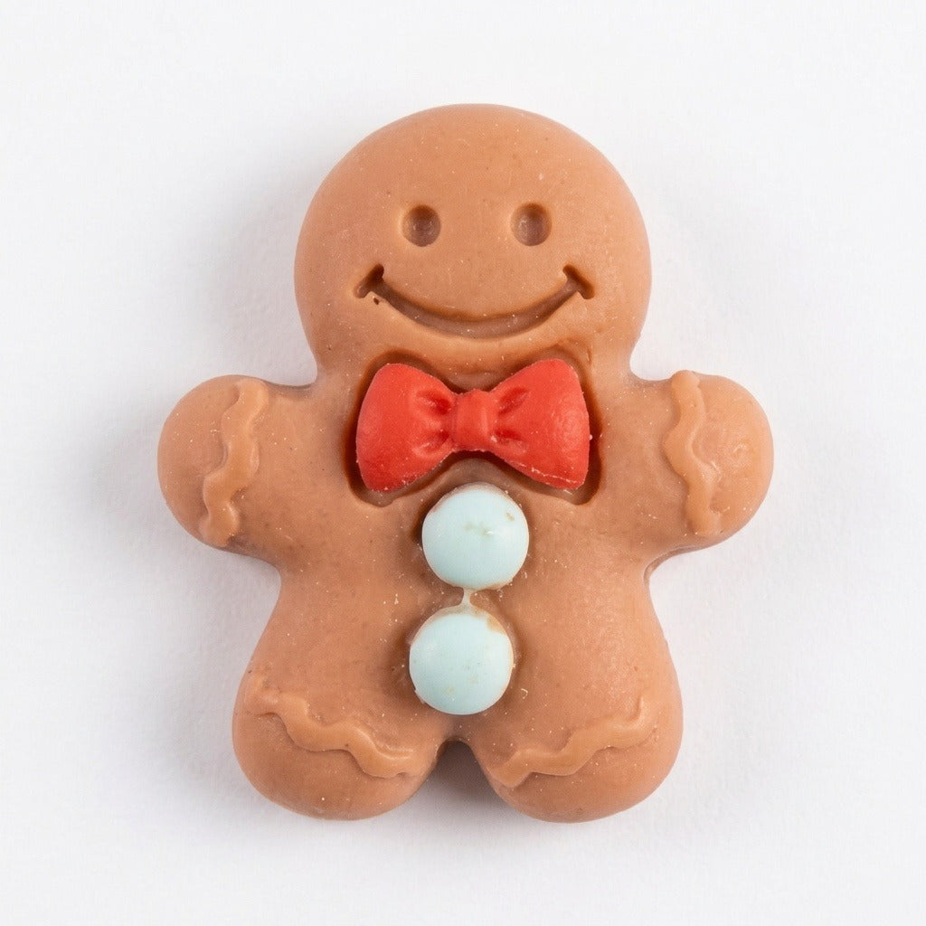 A brown resin gingerbread craft embellishment has a smiling face, red bow tie, and pale blue buttons against white.