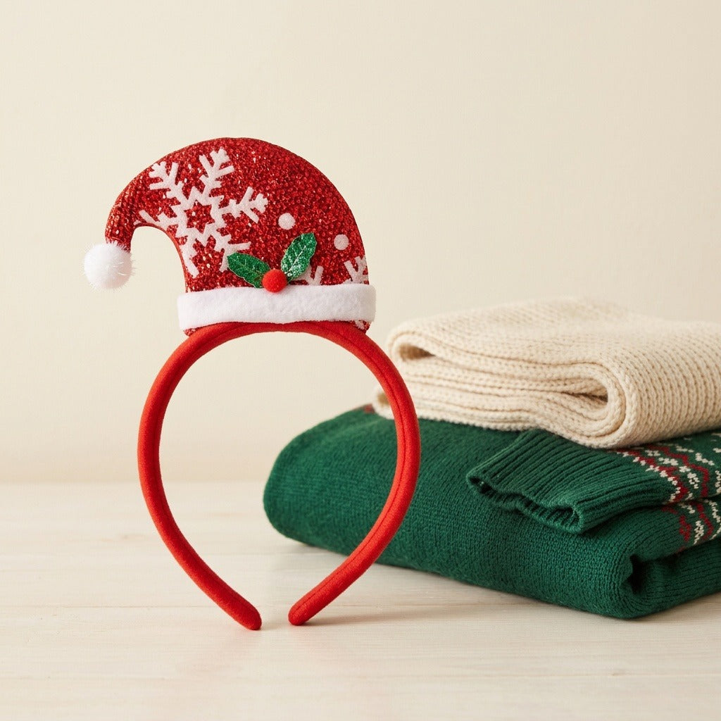A red Christmas headband topped with a glittery Santa hat and white snowflakes stands beside cream and green knitwear.