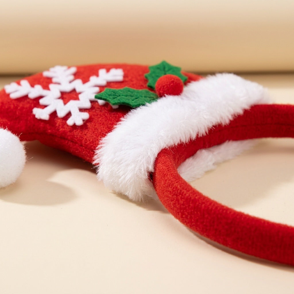 A red fabric Christmas headband rests on a cream surface, showing its Santa hat decoration, fluffy white trim, snowflake, and holly.