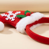 A red fabric Christmas headband rests on a cream surface, showing its Santa hat decoration, fluffy white trim, snowflake, and holly.