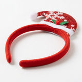 Red fabric Christmas headband with a glittery Santa hat, white snowflakes, fluffy trim, and green holly leaves rests on white.