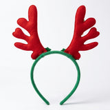 Green fabric Christmas headband with tall red felt-like antlers and small green glitter accents stands upright against a white background.