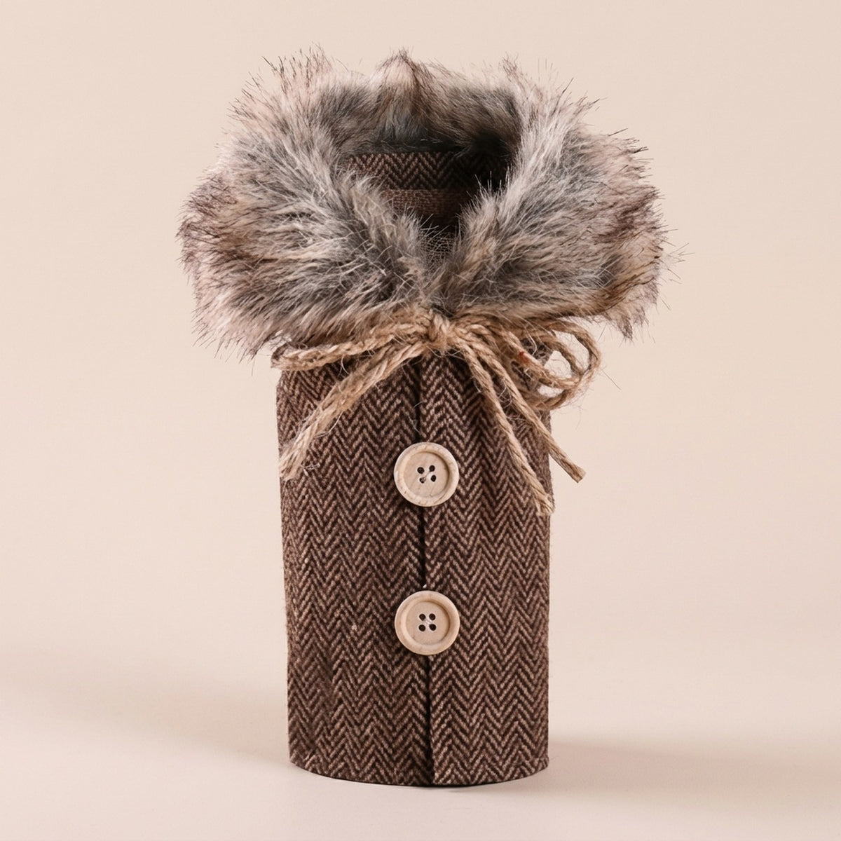 Brown herringbone wine bottle cover has a fluffy gray collar, twine bow and two beige buttons against a pale beige background.
