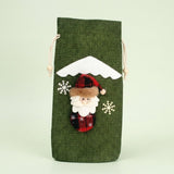 Green textured drawstring wine bottle cover with a Santa appliqué, white snowflakes and snowy roof trim against a pale green background.