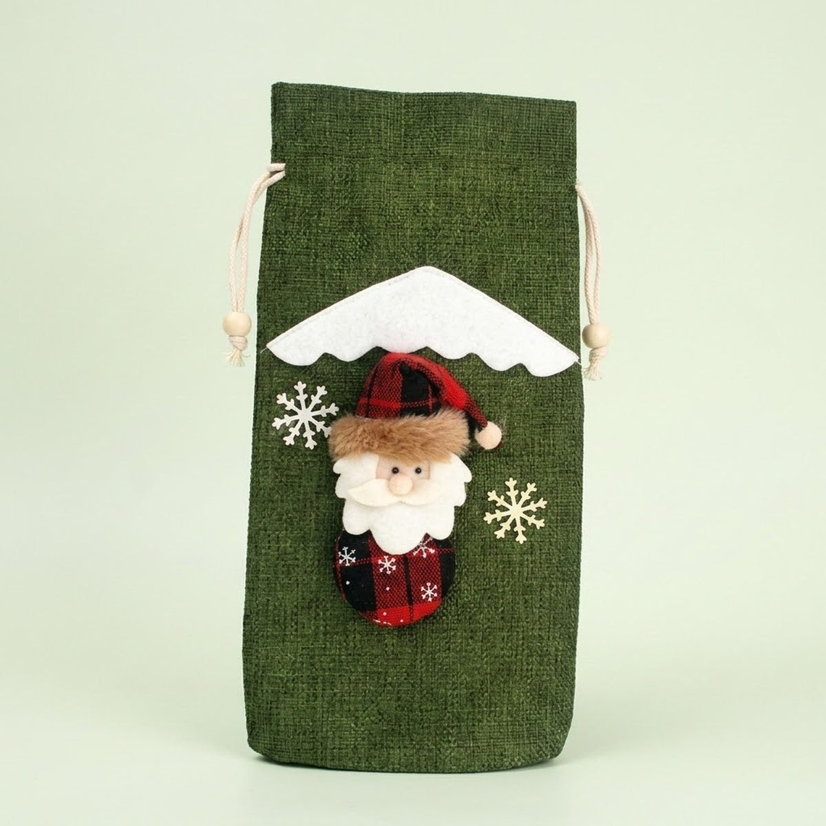 Green textured drawstring wine bottle cover with a Santa appliqué, white snowflakes and snowy roof trim against a pale green background.