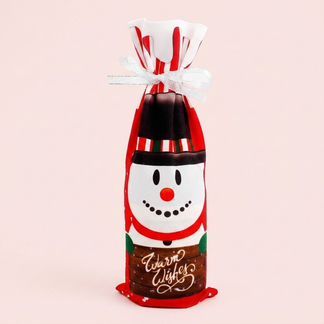 Red cloth wine bottle cover features a snowman print, Warm Wishes lettering and white ribbon against a pale pink background.