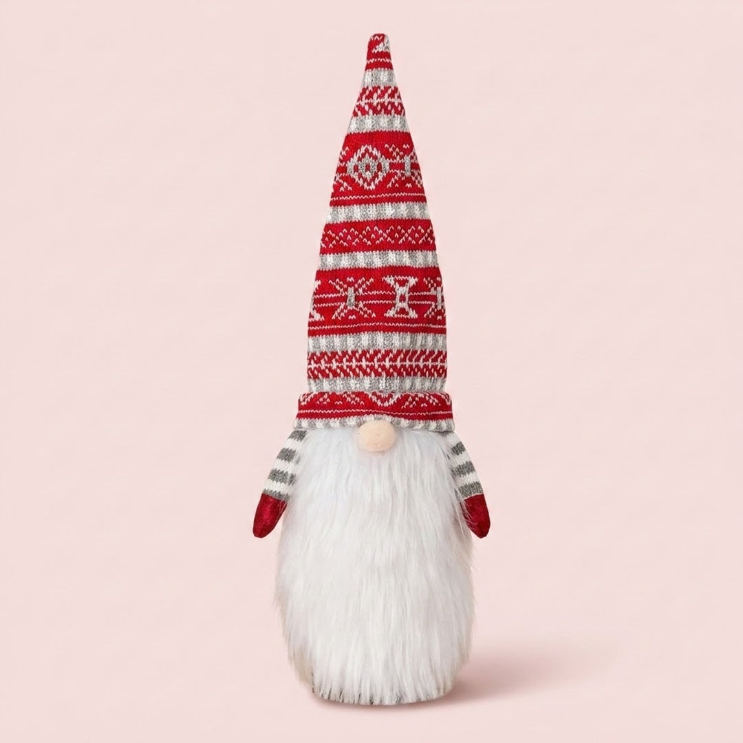 Gnome-style wine bottle cover with a tall red patterned knit hat, white beard and red mittens stands against a pale pink background.
