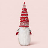 Gnome-style wine bottle cover with a tall red patterned knit hat, white beard and red mittens stands against a pale pink background.
