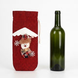 A red woven wine bottle cover with a snowman decoration stands beside an uncovered green glass bottle against a white background.