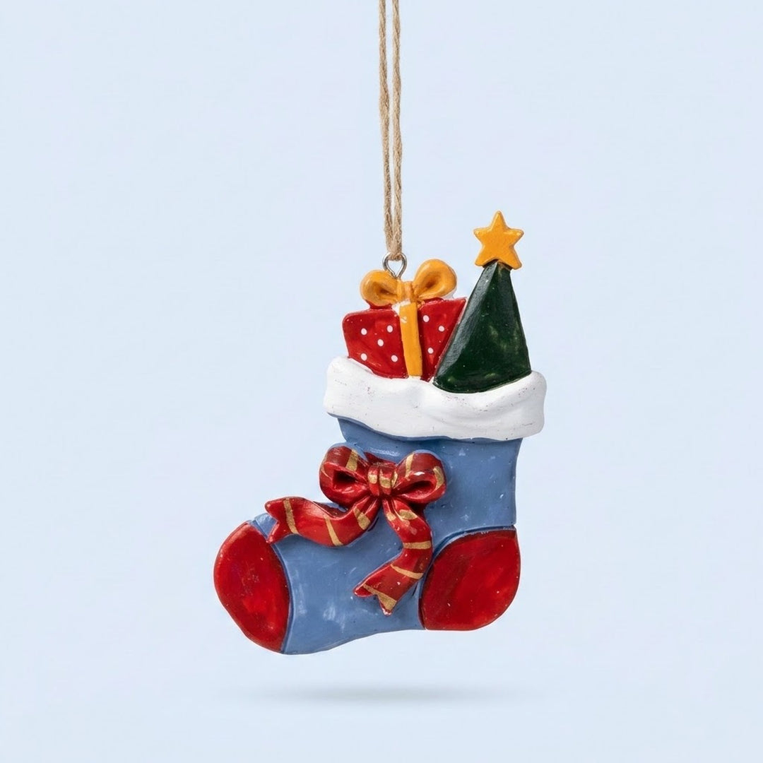 Resin Christmas ornament shaped as a blue stocking with a red bow, wrapped gift and green tree hangs against a pale blue background.