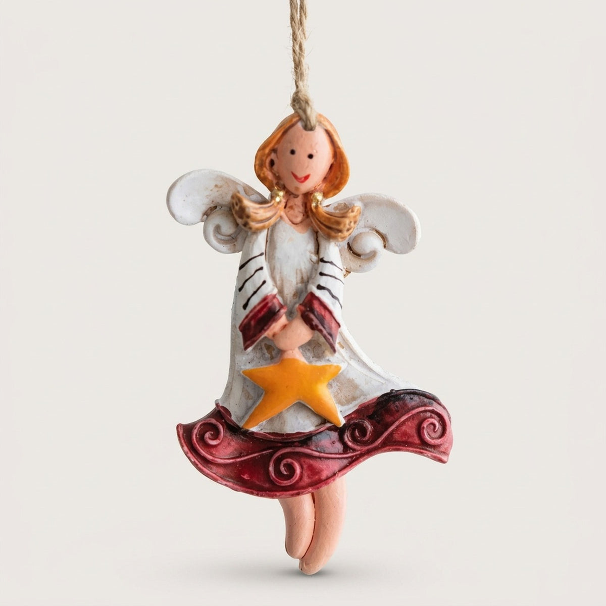 Resin angel Christmas ornament with white wings, burgundy dress trim and a yellow star hangs from twine against an off-white background.