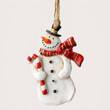 A white snowman Christmas ornament wears a black hat and red scarf, holding a candy cane against an off-white background.