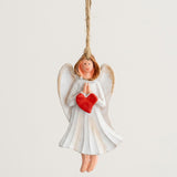 Resin Christmas ornament depicting a white angel with praying hands and a red heart hangs by twine against an off-white background.