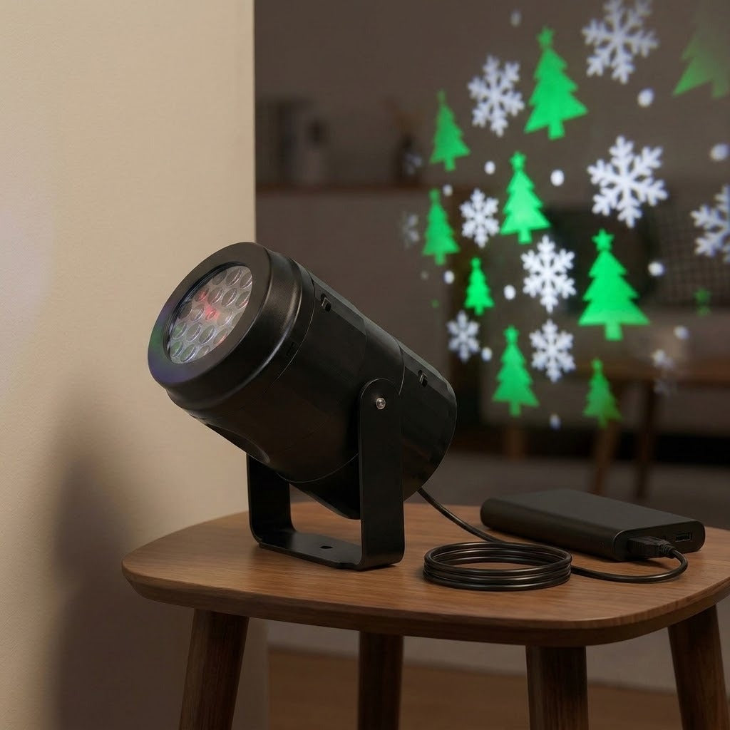 Black Christmas light projector sits beside a power bank on a wooden table, with green trees and white snowflakes projected behind it.