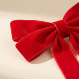 Close-up of a red velvet Christmas bow showing its soft plush texture against a warm off-white background.