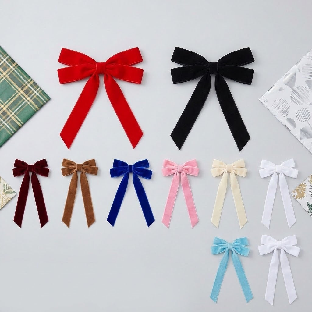 Velvet Christmas bows in assorted colors and sizes lie on a light gray surface beside patterned wrapping paper.