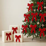 Red velvet bows decorate a Christmas tree with metallic ornaments and warm lights beside three cream gift boxes with matching bows.
