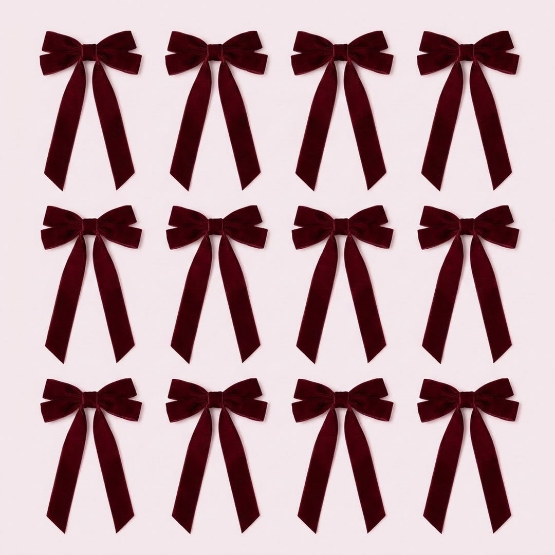 Twelve burgundy velvet Christmas bows with long angled tails are arranged in three rows of four on a pale pink background.