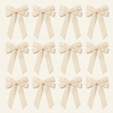 Twelve ivory velvet Christmas bows with long angled tails are arranged in three rows of four on a cream background.