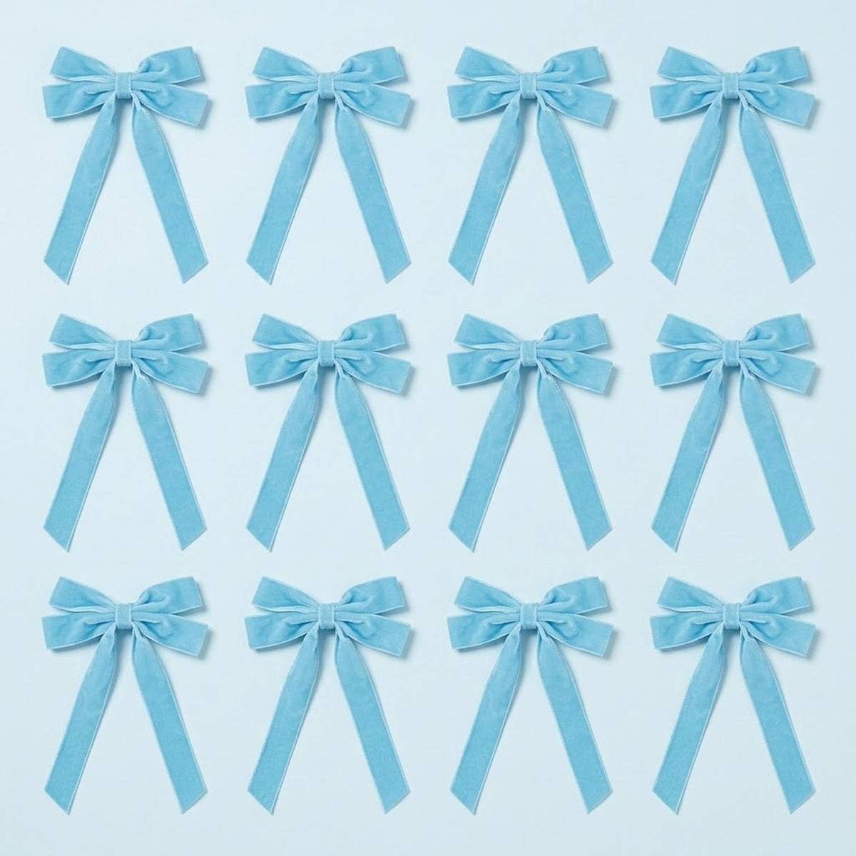 Twelve light blue velvet Christmas bows with long angled tails are arranged in three rows of four on a pale blue background.
